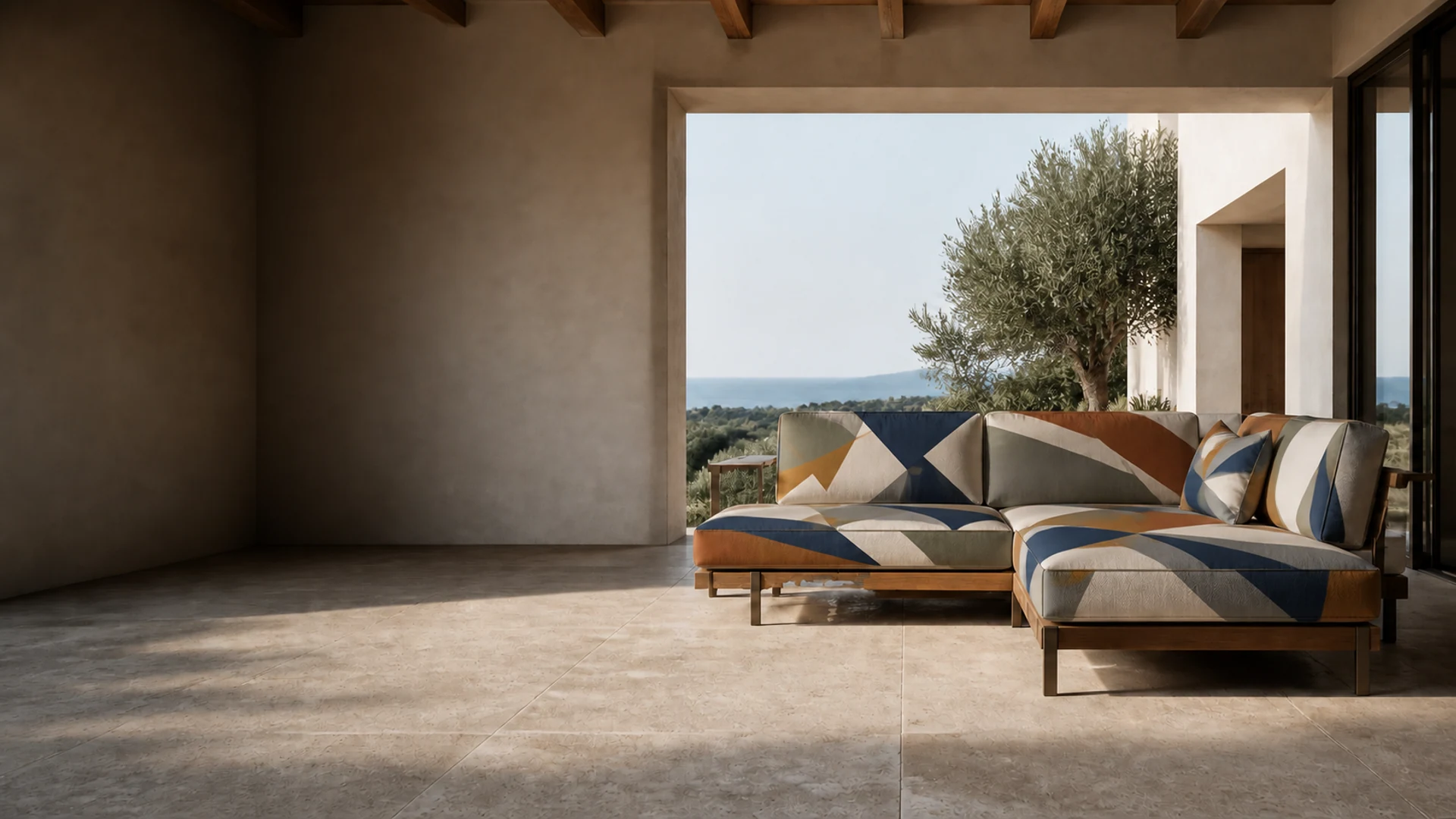 A modular outdoor sofa upholstered in the SOLSTICE design on a covered travertine terrace, with an olive tree and the sea beyond the opening.